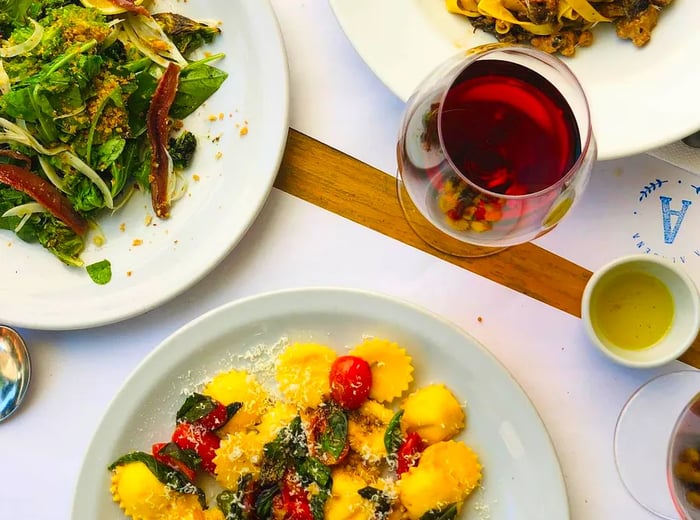 An overhead shot of two plates of pasta, a fresh salad, and a glass of wine