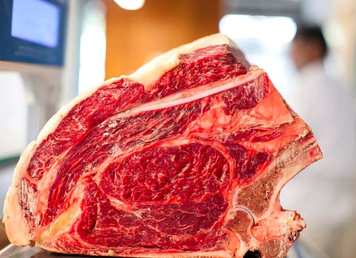 A sizable piece of meat, featuring prominent bones and marbling, rests on a butcher's counter.