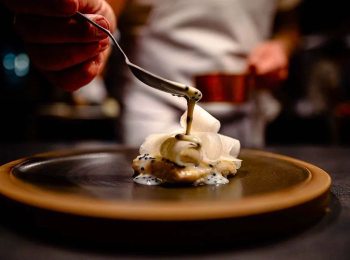 A chef adds a generous dollop of sauce onto a uniquely shaped dish