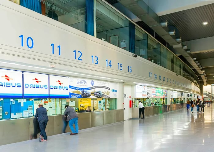 A long row of ticket counters for various bus companies at a large bus station in Madrid, Spain.