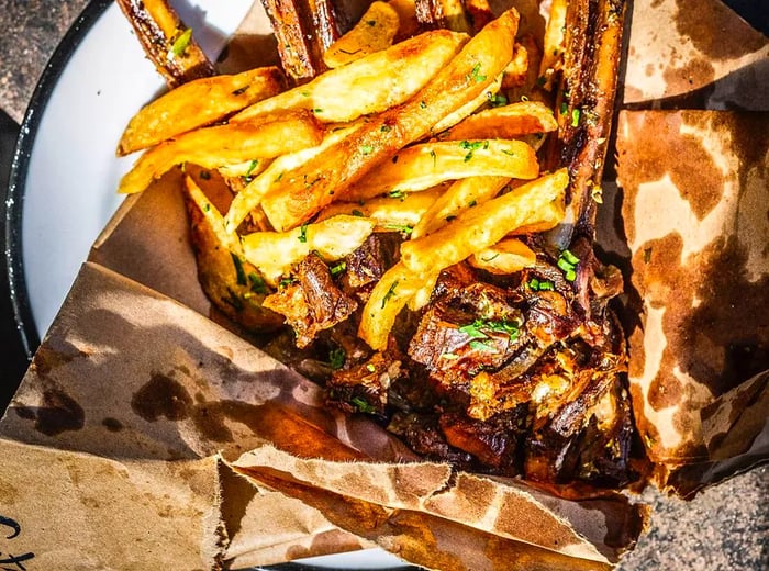 Aerial view of sizable bone-in ribs resting on stained wax paper alongside a generous serving of french fries.