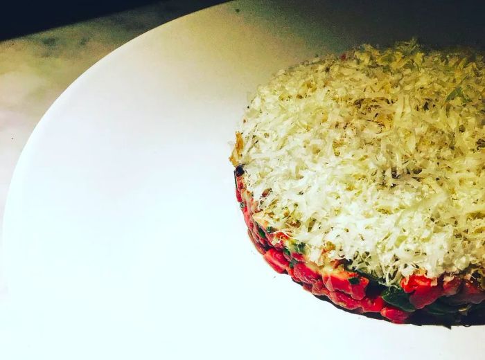 A neatly shaped round of steak tartare garnished with grated cheese on a pristine white plate