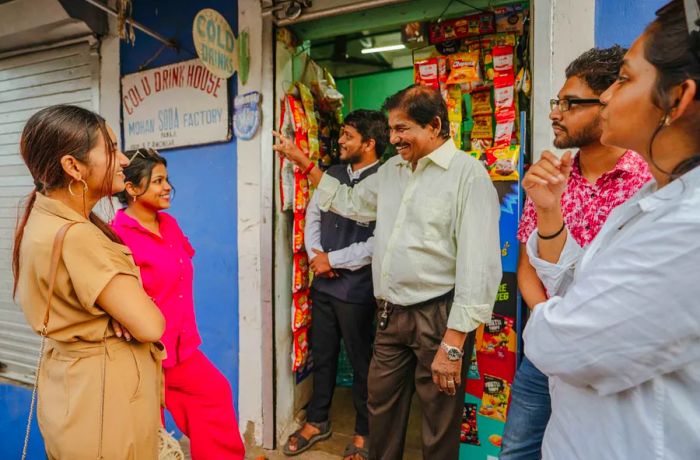 A tour group engages in conversation with a shop owner outside his store.