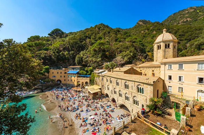 A large crowd of tourists enjoys sunbathing and relaxing on the small beach on a sunny spring day in Genoa, Italy.