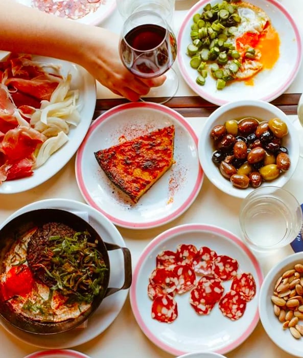 An overhead view of a table laden with an array of dishes, including charcuterie, olives, nuts, and Spanish tortilla