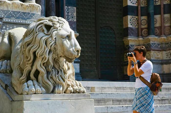 A woman capturing a photo of a lion statue outside the cathedral in Genoa.