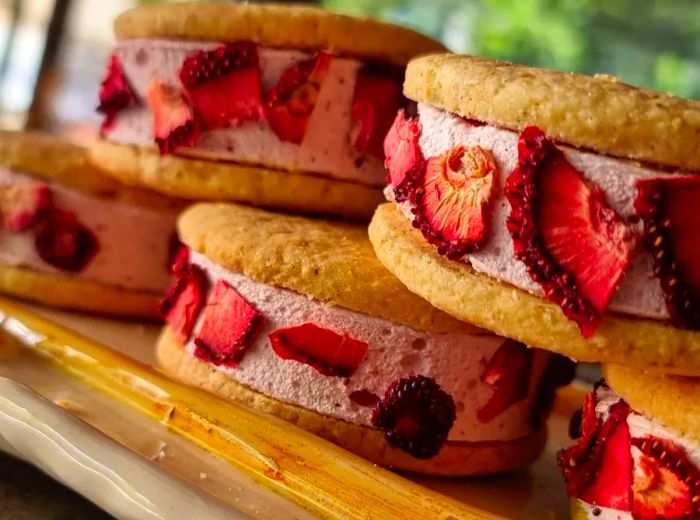 Alfajores filled with pink cream, encased in blond cookies and adorned with slices of dried strawberries on the outside.