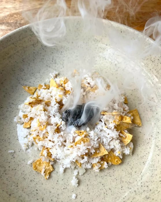 A plate of rice paired with crispy torn papad (wafers), emitting a smoky aroma from a coal fire in the center.