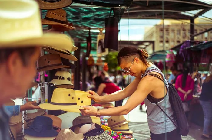 A person in a vest and sunglasses browses a selection of cowboy hats at an open-air market in Guadalajara