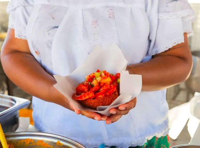 A chef proudly displays an acarajé filled to the brim with shrimp and toppings.