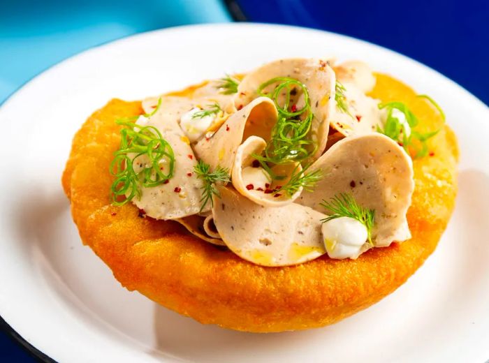 A small round of fried dough garnished with mortadella and herbs.