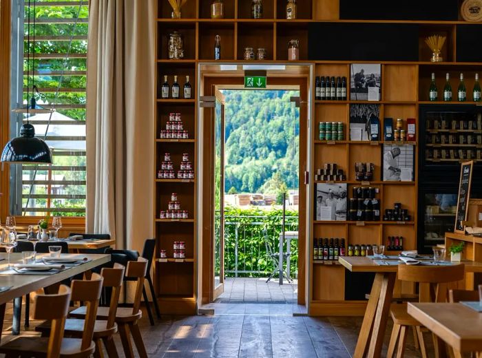 A restaurant interior featuring a wall lined with shelves filled with various kitchen items, and a door that opens to the lush landscape outside.