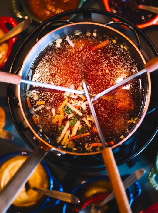 A stew pot with skewers resting in the flavorful broth.