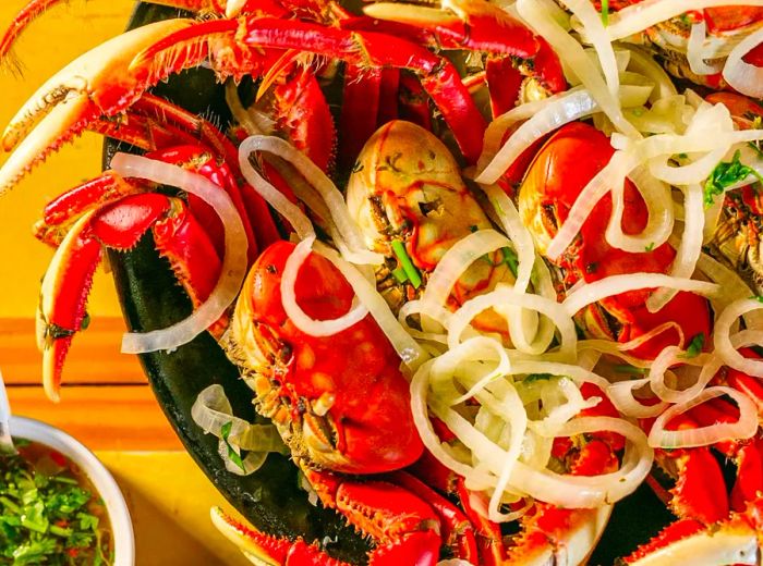 Vibrant red whole crabs topped with grilled onions, accompanied by a variety of side dishes.