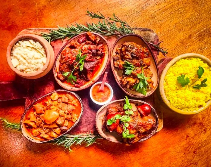 A large wooden board on a table displaying several ceramic pots filled with various stews and rice dishes.