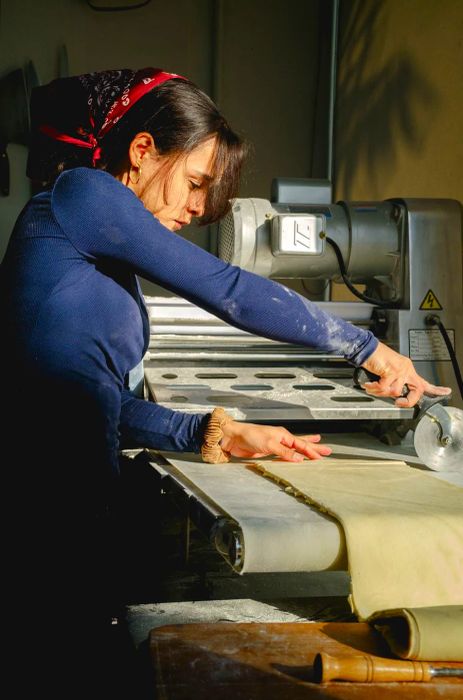 A pastry chef uses a rolling cutter to slice through dough.