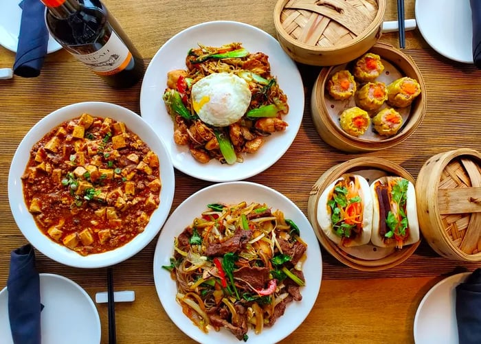 Steamer baskets filled with dumplings and buns, accompanied by plates of mapo tofu and other delicacies.