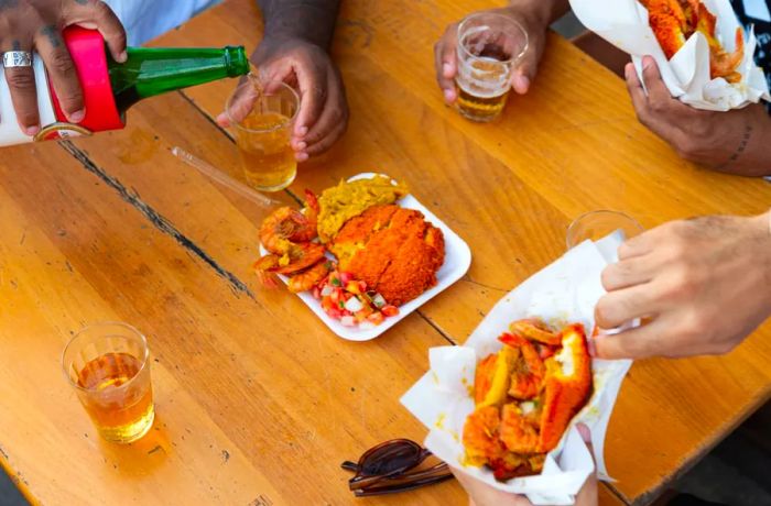 Diners at a wooden patio table enjoy acarajés and sip on beer.