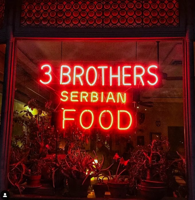 A bright neon sign stating “3 Brothers Serbian Food.”