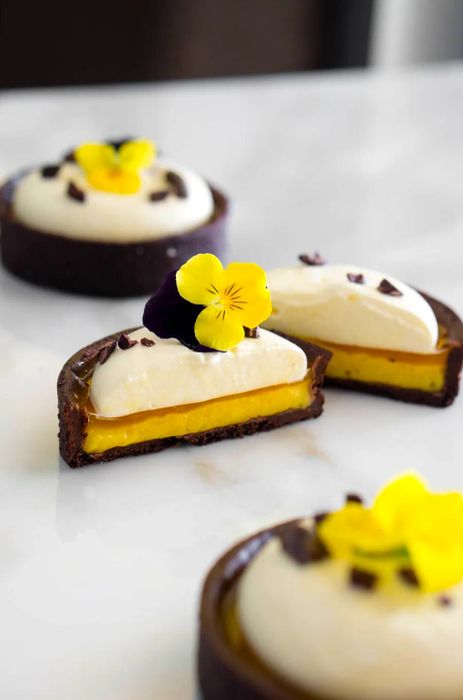 A tart sliced in half, showcasing its layers of chocolate base, vibrant yellow passion fruit filling, and a creamy topping.