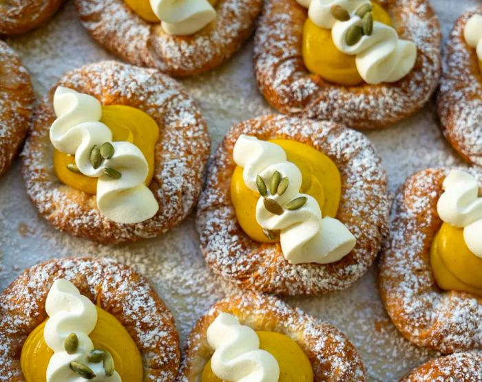 A close-up of neatly arranged tarts adorned with swirls of cream.