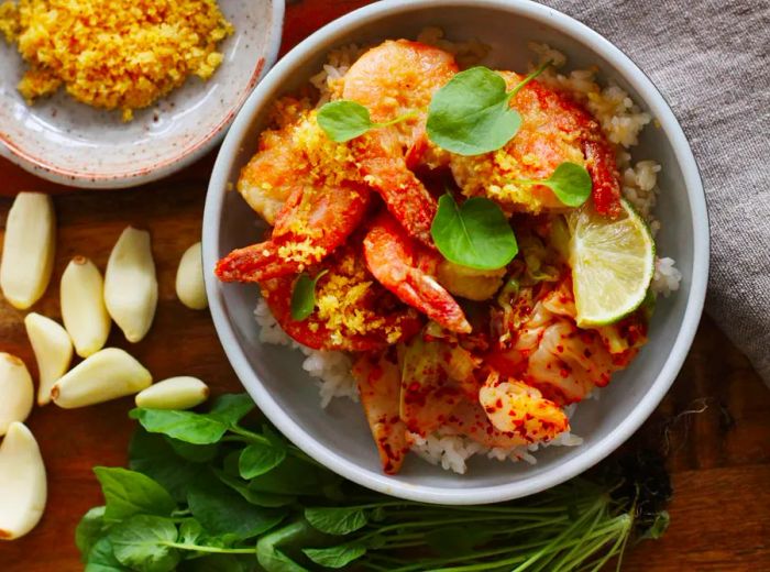 Aerial view of a bowl filled with garlic shrimp over rice, accompanied by nearby ingredients.