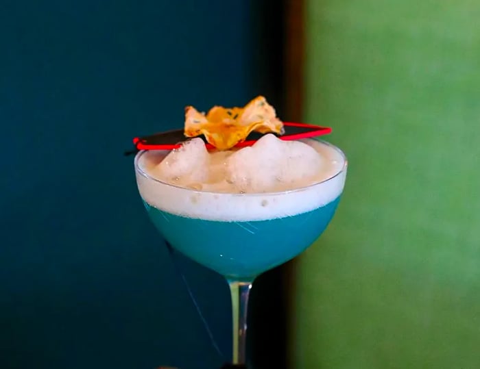 A vibrant blue cocktail with a frothy top and a whimsical garnish.