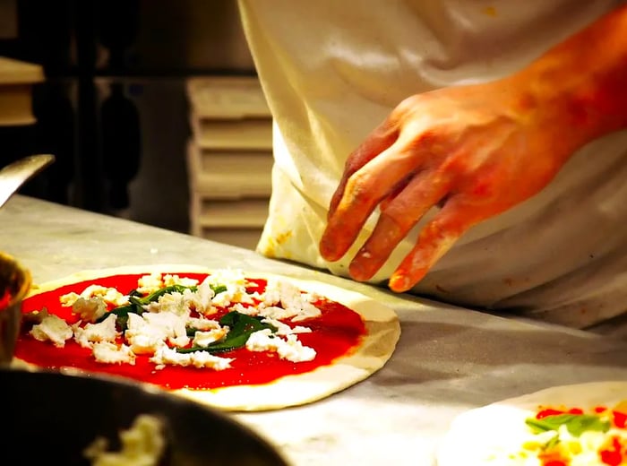 A chef assembles a pizza by adding toppings to an unbaked crust.