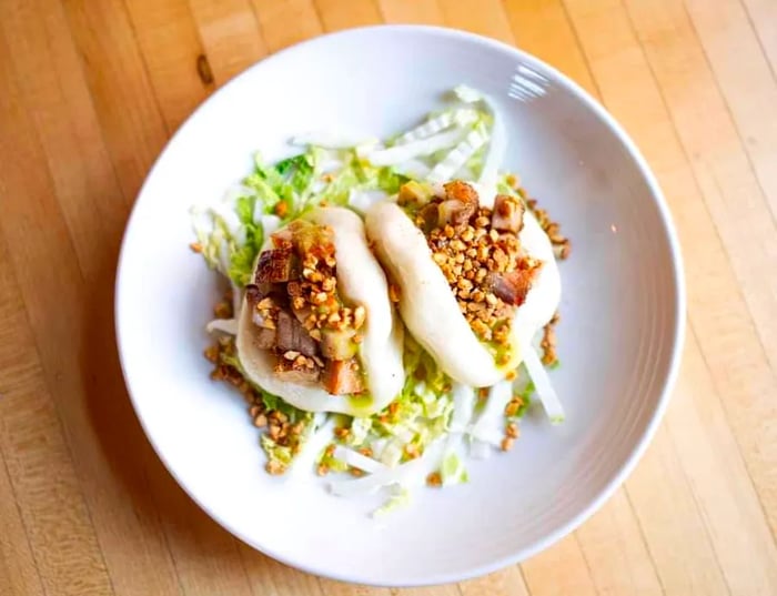 A pair of pork buns nestled on a bed of chopped lettuce, adorned with crunchy toppings.