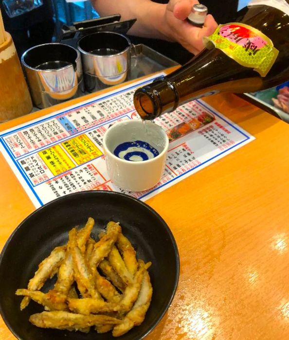 A person pours sake beside a snack.