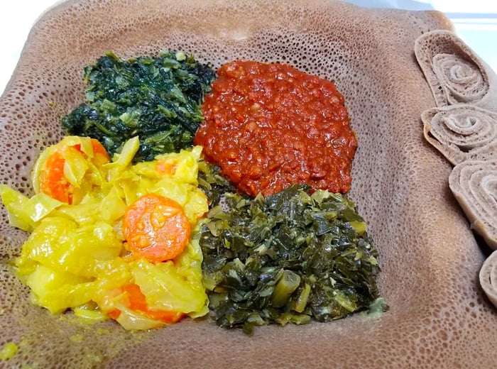 A takeout container filled with injera topped with cabbage, spinach, collards, and red lentils.