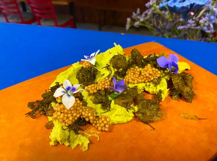 A vibrant display of cooked vegetables atop a green asparagus pate, embellished with mustard seeds and edible flowers.