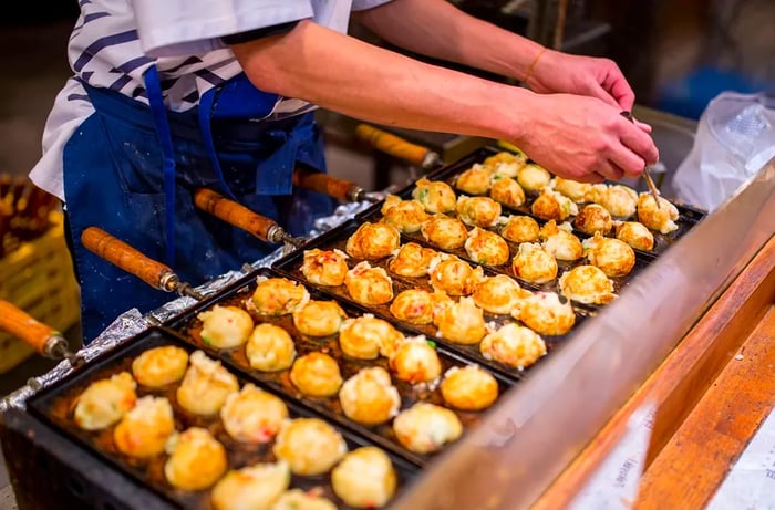 A chef skillfully flips takoyaki in a specialized pan designed for molding.