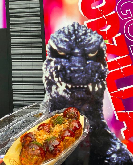 A plate of takoyaki set against a vintage Godzilla movie poster.