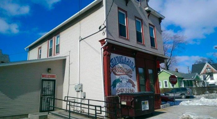 A two-story shingled structure featuring a brownstone facade on the lower level, adorned with a large illustrated paper sign for Guadalajara Restaurant.