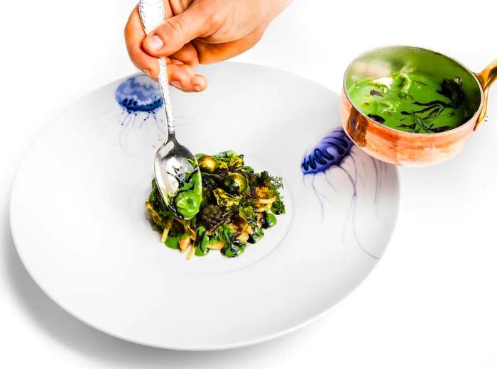 A hand ladles sauce from a gleaming copper pot onto a beautifully crafted dish