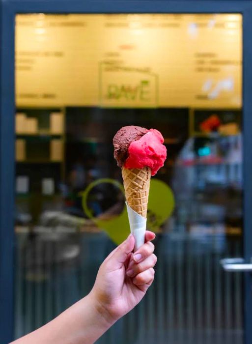 A hand holds a cone filled with two delicious gelato flavors.