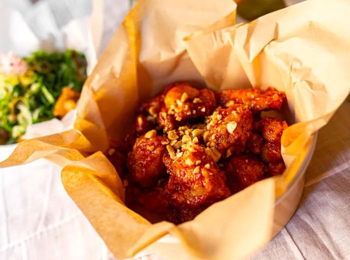 A bowl lined with butcher paper filled with popcorn fried chicken, garnished with chopped nuts and sauce