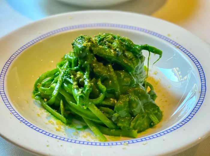 Noodles drizzled with a rich green sauce, elegantly presented on a decorative plate.