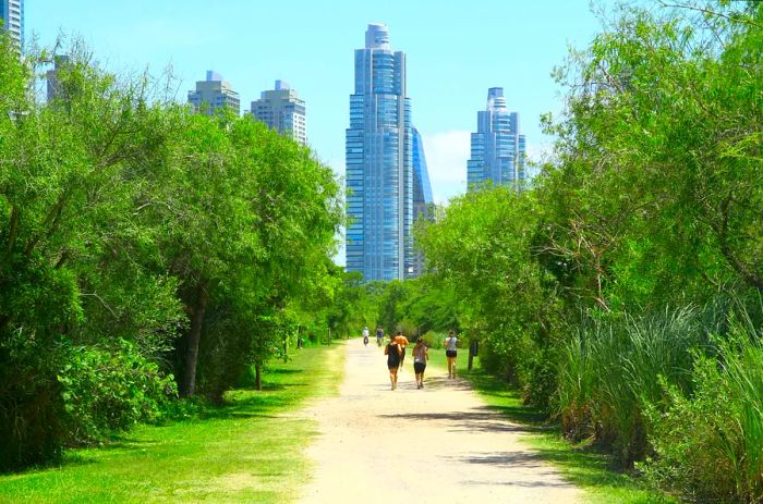 Joggers and walkers enjoy a dirt path at Reserva Ecológica Costanera Sur, framed by the Buenos Aires skyline.