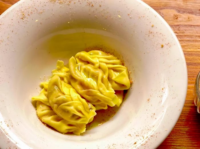 Beautifully braided tortelli pasta served in a shallow bowl alongside a small glass of grated cheese.