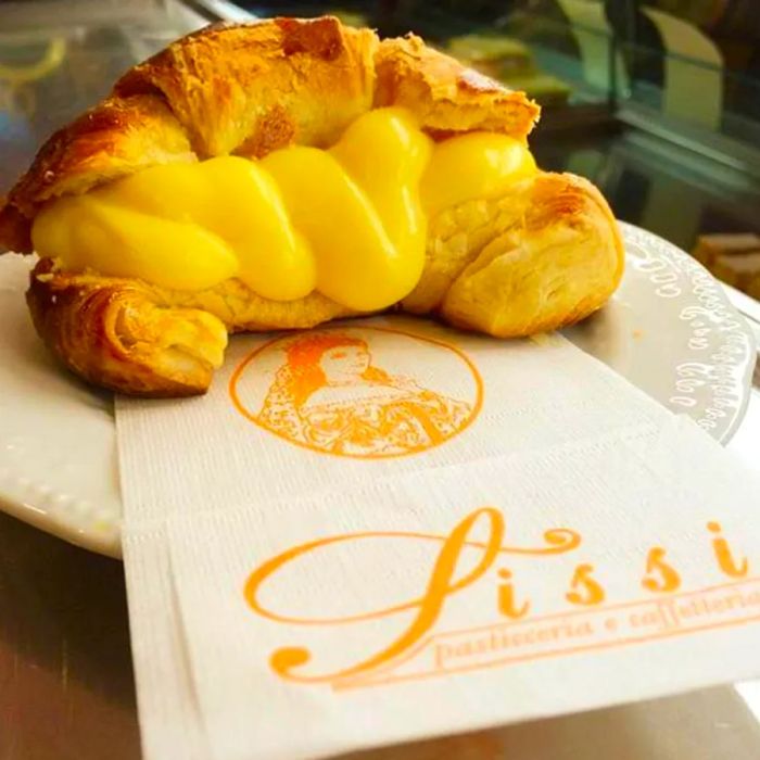 A golden croissant filled with creamy yellow filling, resting on a branded napkin.