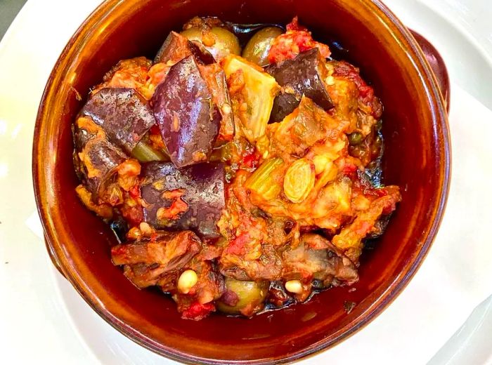 An overhead view of a glazed clay bowl filled with vibrant caponata, featuring particularly vivid purple eggplant.