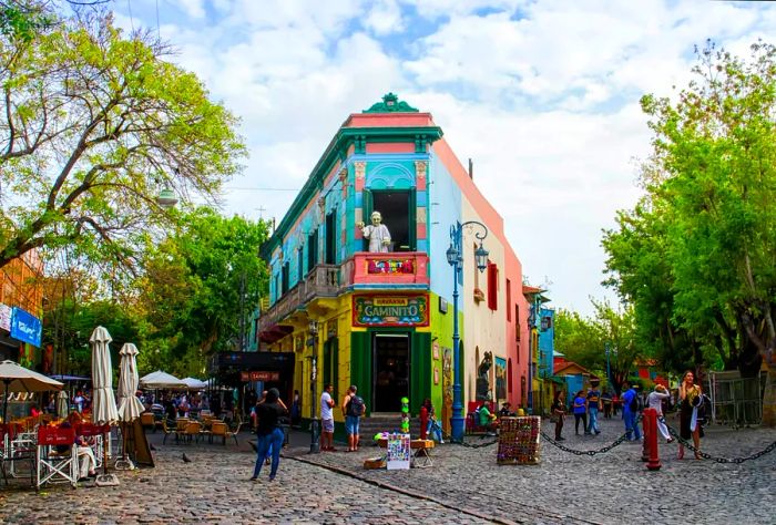 A strikingly colorful building stands out on a quaint pedestrian street filled with stalls and cafes.