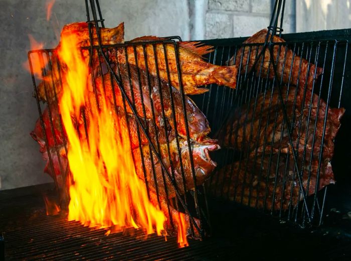 Grill baskets filled with several fish cooking over open flames.