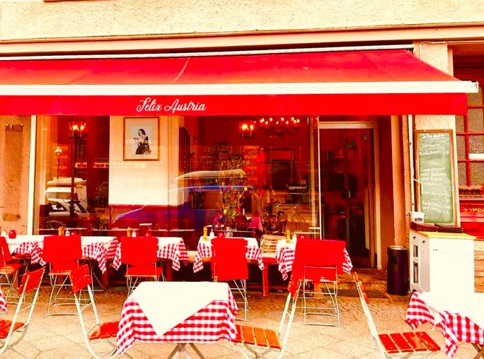 A restaurant facade adorned with a vibrant red awning and matching patio seating.