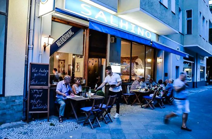 An inviting restaurant facade featuring diners enjoying their meals at quaint picnic tables along a cobblestone street.