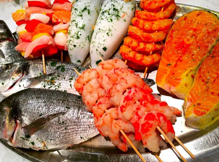 A beautifully arranged platter featuring whole fish, fish steaks, and skewered seafood, perfect for grilling.