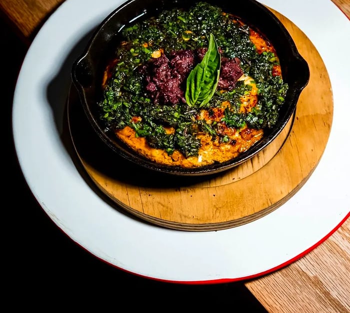 A cast iron skillet filled with cheese drizzled with chimichurri.