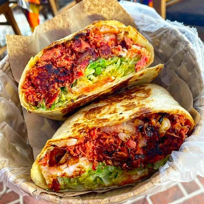 A burrita filled with a vibrant red seafood mixture, guacamole, and other fresh ingredients, sliced open to showcase its contents.